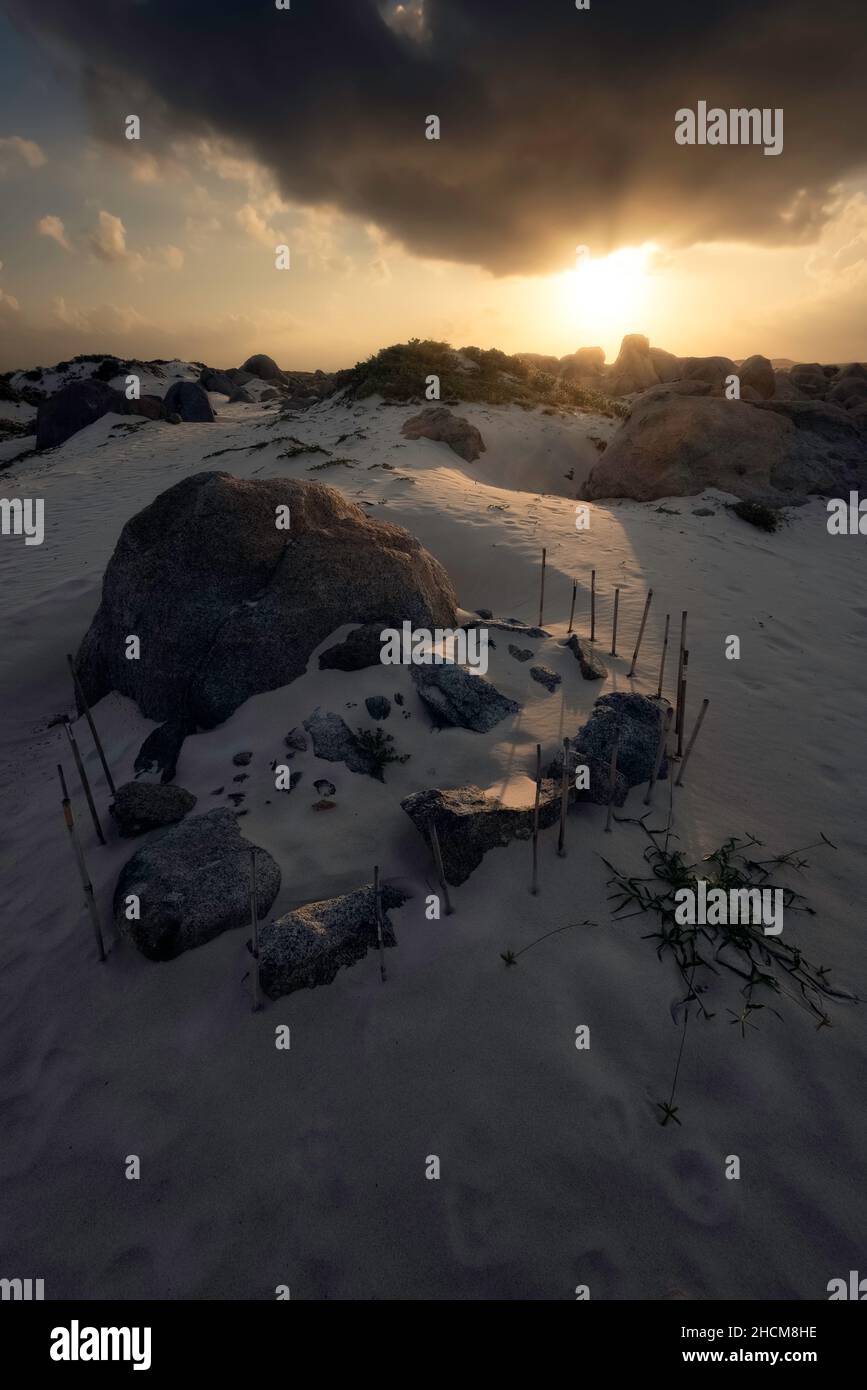 Sonnenaufgang auf den Arashi Dunes von Aruba mit einer geheimnisvollen Formation von Stöcken und Steinen im Sand. Stockfoto