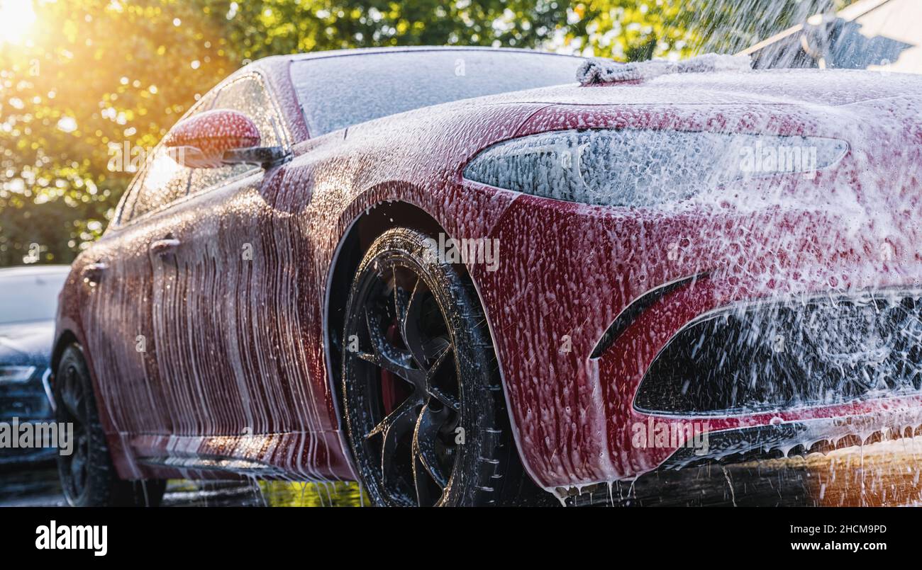 Sprühen von Schaum auf ein rotes Auto mit Hochdruckschaum Pistole Autowäsche bei Waschservice Stockfoto