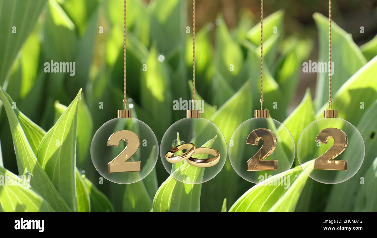 goldene Eheringe in Glaskugel mit 2022 Ziffern und schönen grünen Blättern mit Tau-Tropfen Hintergrund Stockfoto