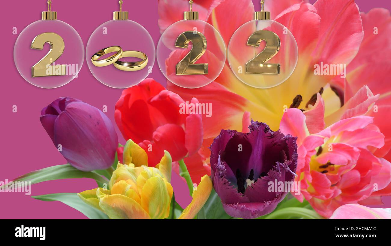 goldene Eheringe in durchsichtiger Glaskugel mit 2022 Ziffern und einem bunten Frühlingsstrauß im Hintergrund Stockfoto