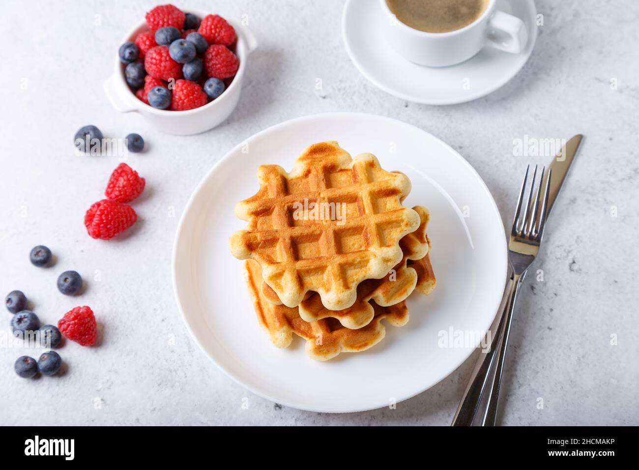 Wiener oder belgische Waffeln mit frischen Beeren (Himbeeren und Blaubeeren) auf einem weißen Teller und einer Tasse Kaffee. Traditionelles Dessert. Nahaufnahme, Whit Stockfoto