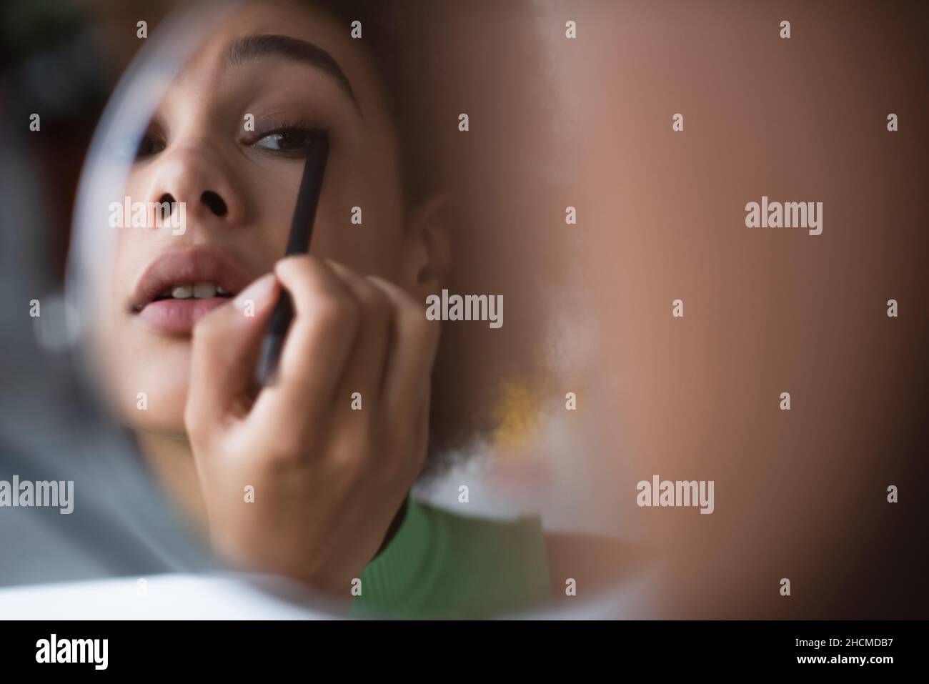 afroamerikanische Frau, die Eyeliner in der Nähe des Spiegels anwendet Stockfoto