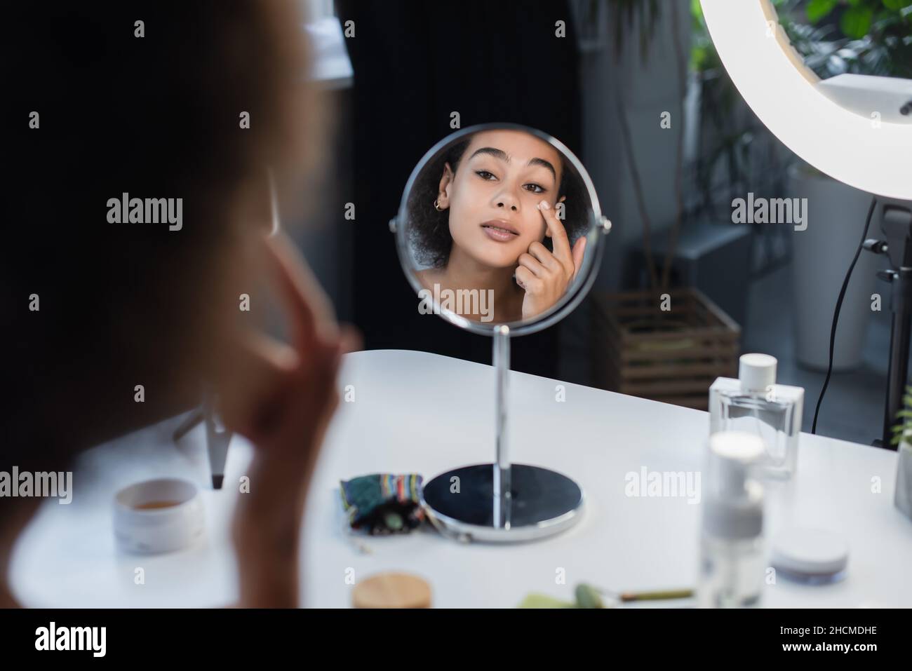 Verschwommene afroamerikanische Frau, die Kosmetikcreme in der Nähe von Spiegel und Parfüm zu Hause anwendet Stockfoto