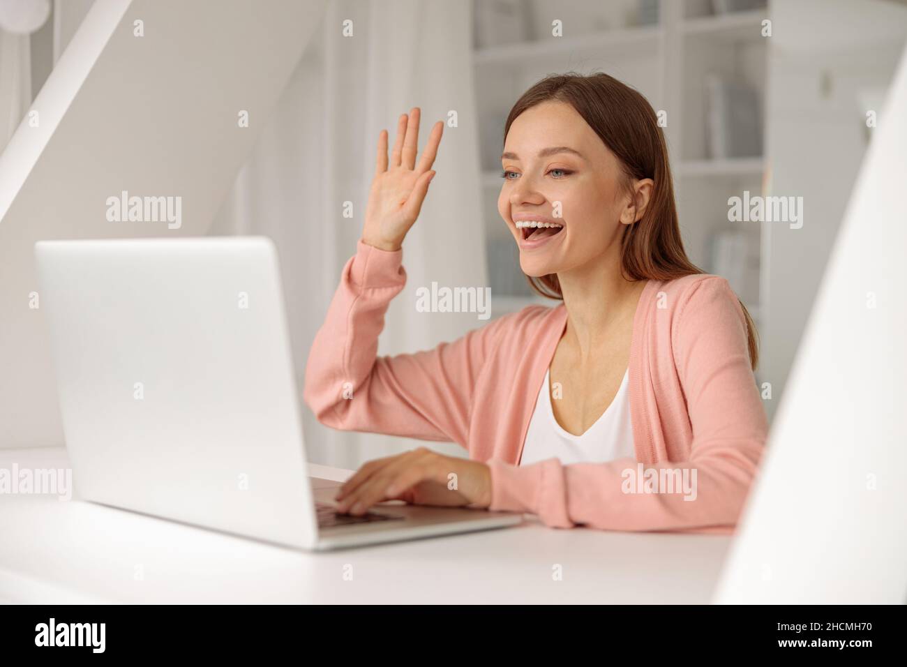 Lächelnde, hübsche Frau, die während eines Videoanrufs einen Laptop benutzt Stockfoto