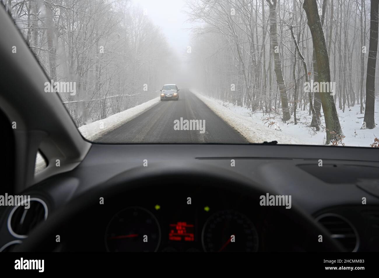 Gefährliche Wintersaison mit Schnee auf der Straße. Der Innenraum des Autos aus Sicht des Fahrers - gefährlicher Verkehr bei schlechtem Wetter. Stockfoto