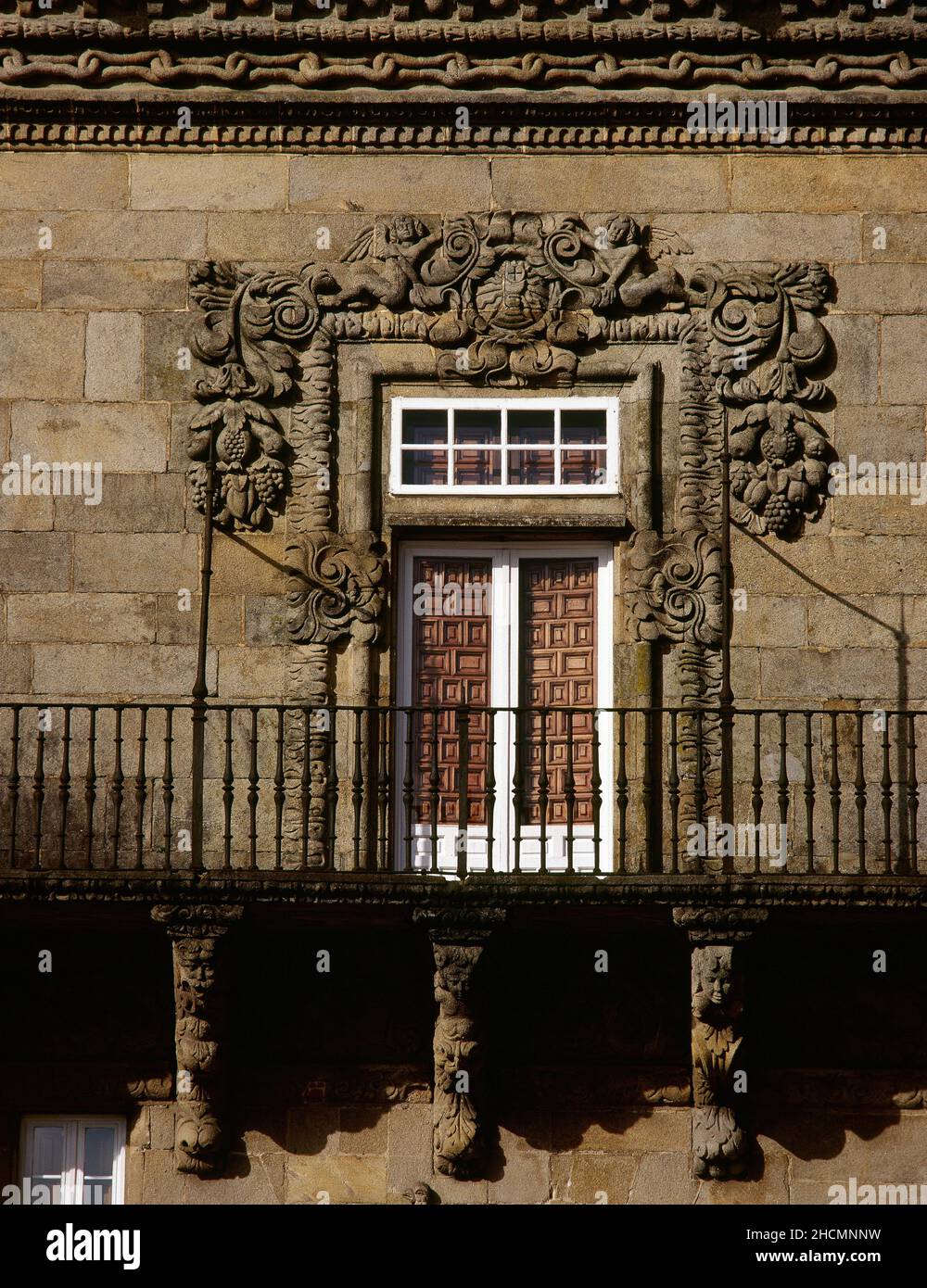 Spanien, Galizien, Provinz Coruña, Santiago de Compostela. Hostal de Los Reyes Católicos (Catholic Monarchs Hostel). Das ehemalige königliche Krankenhaus, das 1501 von den katholischen Königen erbaut wurde, um Kranke und Pilger auf dem Weg nach Compostela zu versorgen. Detail eines der Balkone an der Hauptfassade, entworfen vom Benediktiner-Mönch Tomás Alonso, mit dem Fenster, das von skulpturalen Reliefs mit Trauben (17th. Jahrhundert) eingerahmt wird. Stockfoto