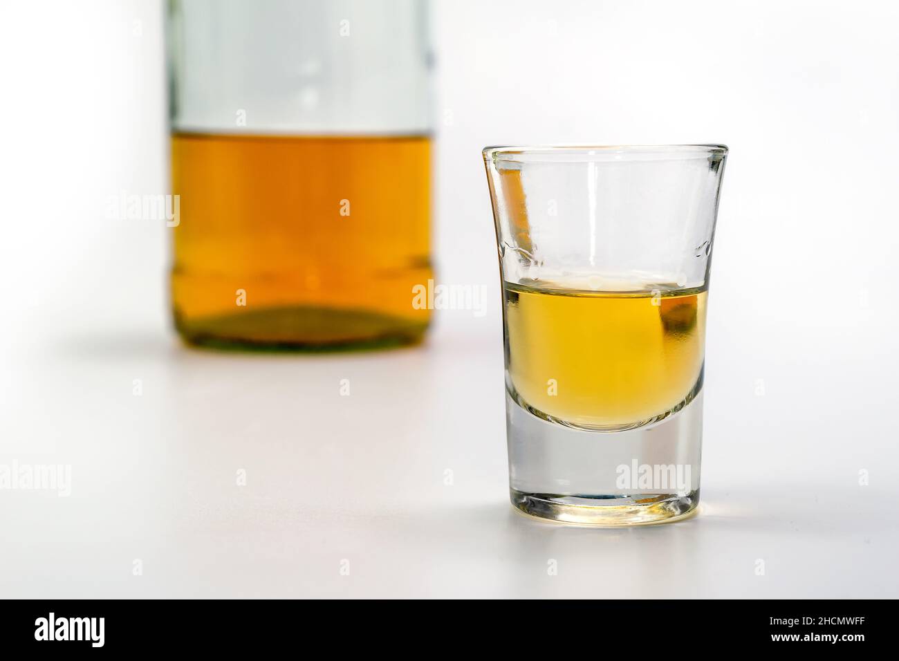 Alkoholisches Getränk in einem Glas und eine Flasche Brandy auf der Rückseite auf dem weißen Tisch. Starker Alkoholvergiftung. Das Konzept der Alkoholabhängigkeit. Alcoh Stockfoto