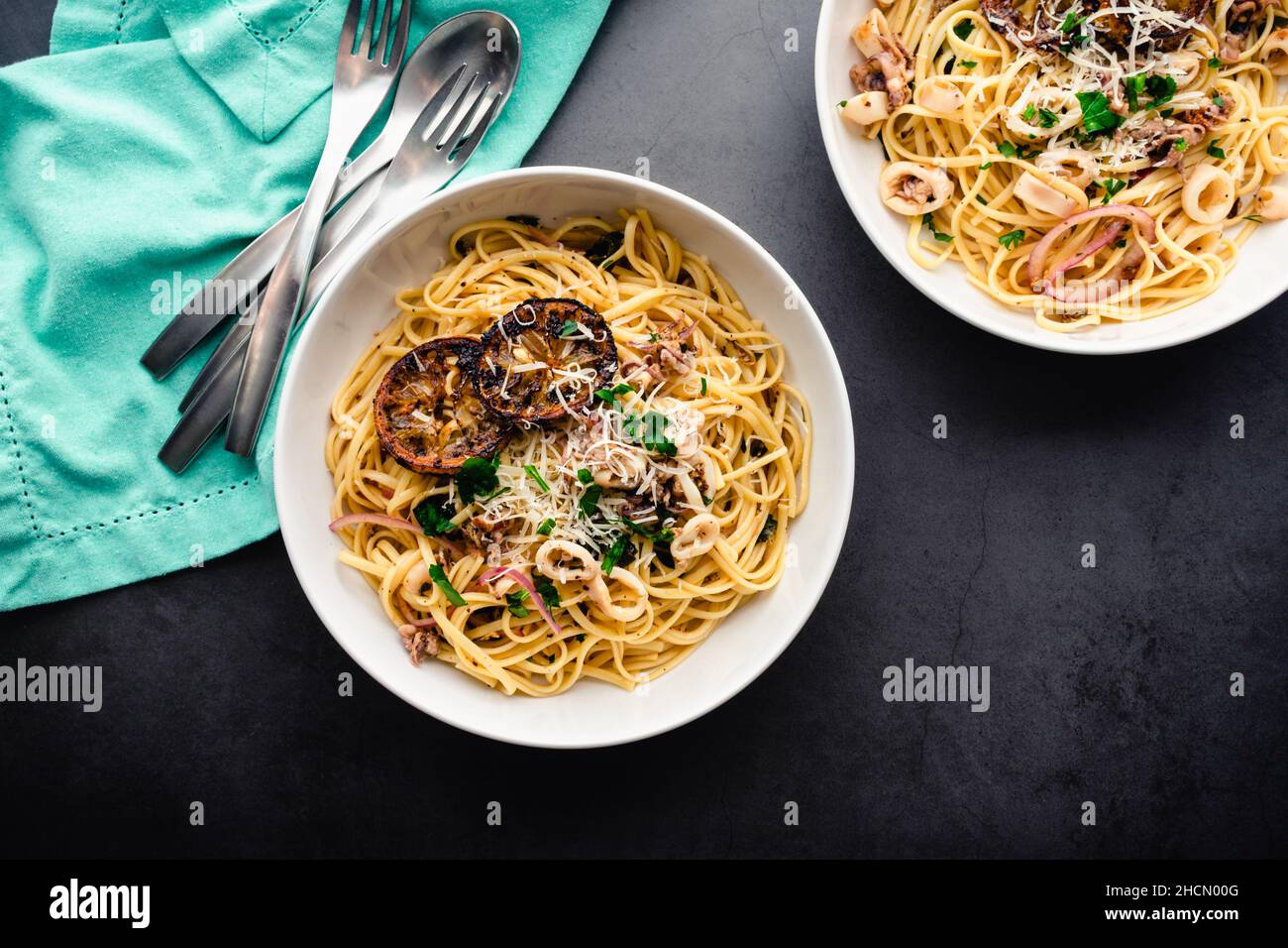 Draufsicht auf Squid Piccata garniert mit verkohlten Zitronenscheiben: Schalen mit Tintenfisch Piccata aus Linguin-Nudeln Stockfoto