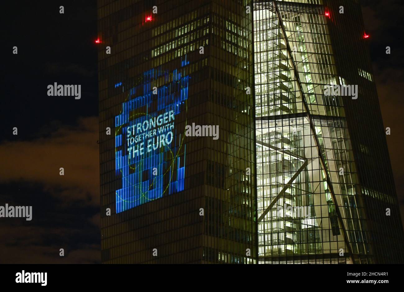 30. Dezember 2021, Hessen, Frankfurt/Main: Bei einem Testlauf wird die Aufschrift „Sronger together with the Euro“ auf die Südfassade des Hauptquartiers der Europäischen Zentralbank (EZB) im Frankfurter Ostende projiziert. Vor 20 Jahren wurde am Silvesterabend in zwölf EU-Ländern die einheitliche europäische Währung, der Euro, eingeführt. Für Deutschland bedeutete dies, Auf Wiedersehen zur D-Mark zu sagen. Vom 31. Dezember 2021 bis zum 9. Januar 2022 wird die Fassade der EZB in den Abendstunden beleuchtet. Foto: Arne Dedert/dpa Stockfoto