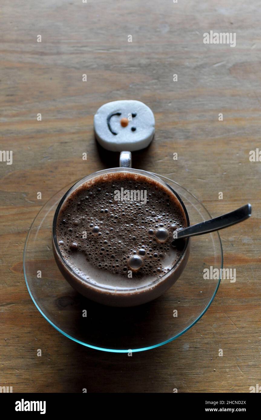 Eine heiße Schokolade in einem Glas Becher mit Untertasse und einem Schneemann Gesicht Marschmalow Stockfoto