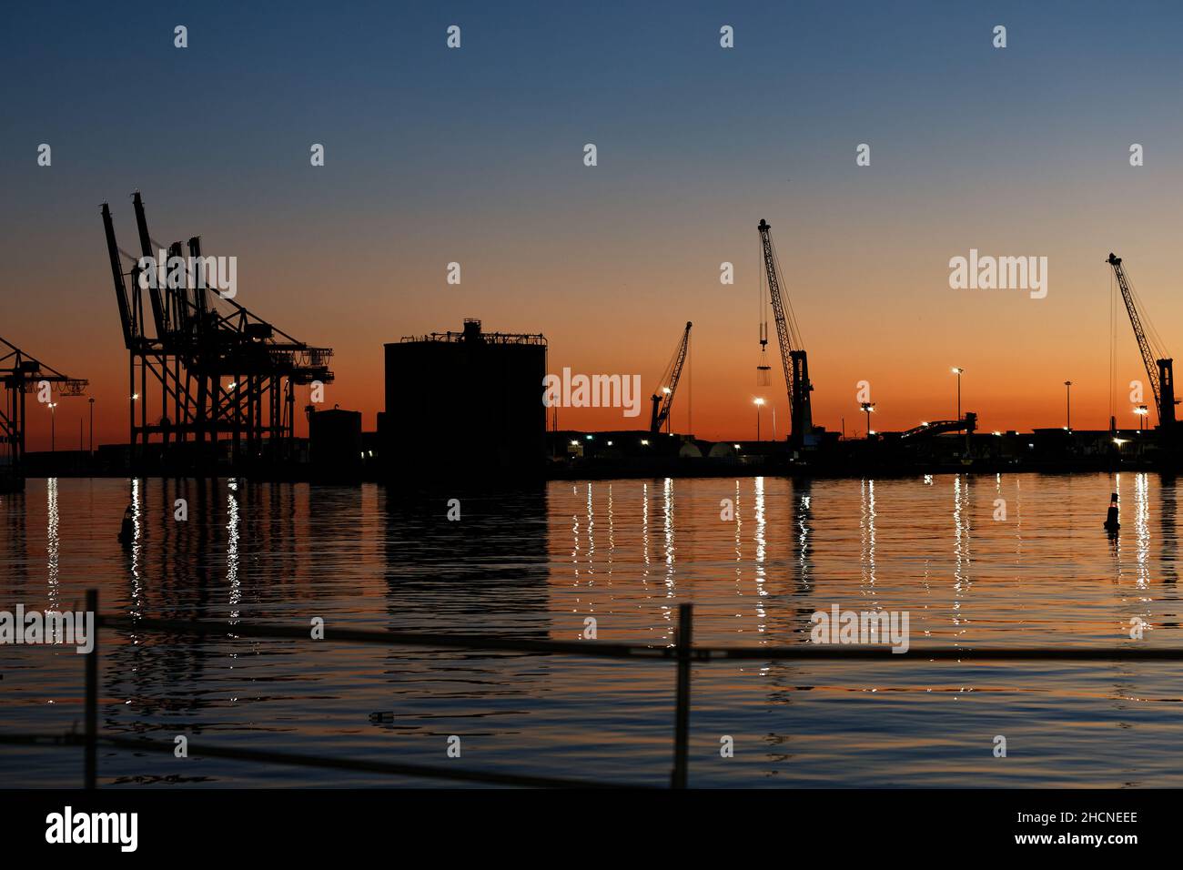 Sonnenuntergang mit Silhouette Industriekranen im Hafen von Málaga (Spanien, November 2021) Stockfoto