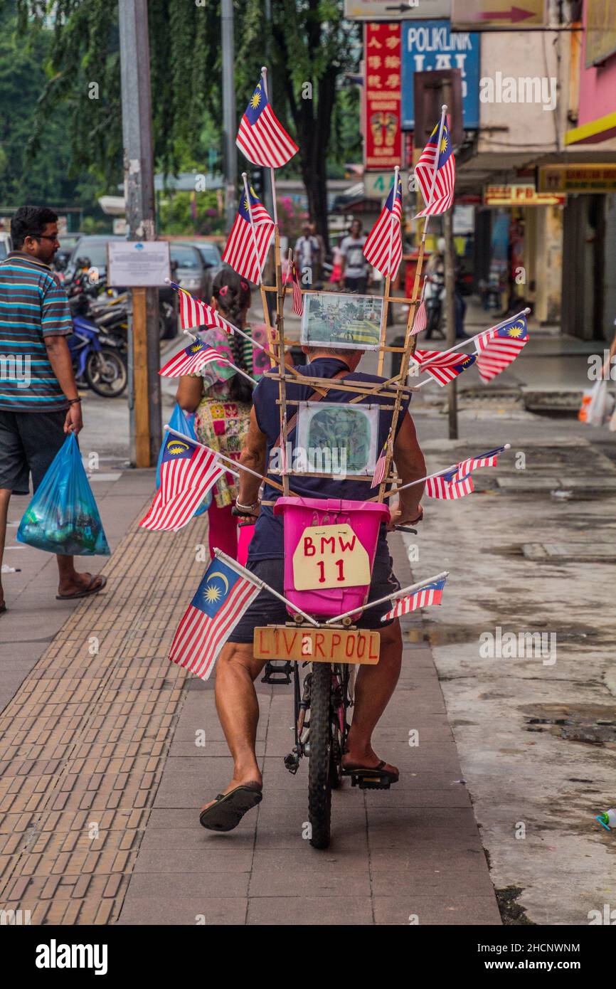 KUALA LUMPUR, MALAYSIA - 31. MÄRZ 2018: Mann auf dem Fahrrad mit malaysischen Flaggen in der Nachbarschaft von Brickfields in Kuala Lumpur, Malaysia. Stockfoto