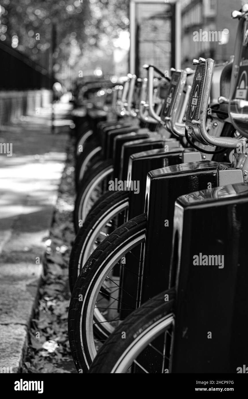 Vertikale Aufnahme einer Reihe von Leihfahrrädern, die in der Nähe des Bürgersteiges geparkt sind, Graustufen Stockfoto
