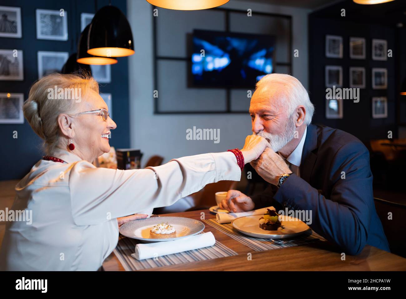 Ein älterer Herr küsst sich während des romantischen Abendessens in einem Restaurant die Hand seiner Frau Stockfoto