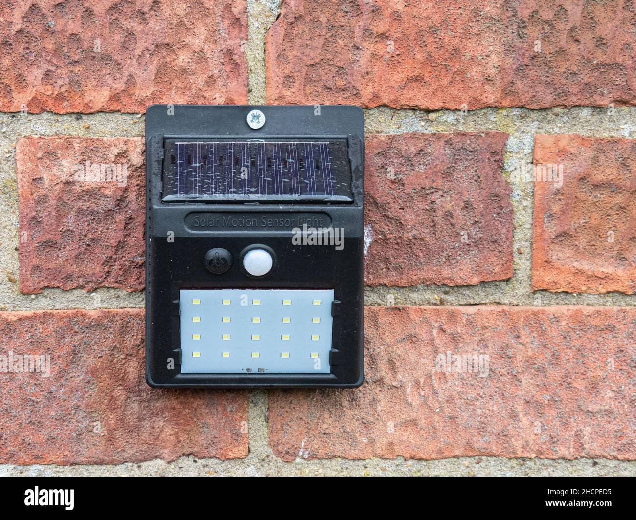 Ein solarbetriebenes Bewegungssensor-Licht mit einem LED-Array, das an einer Ziegelwand befestigt ist Stockfoto