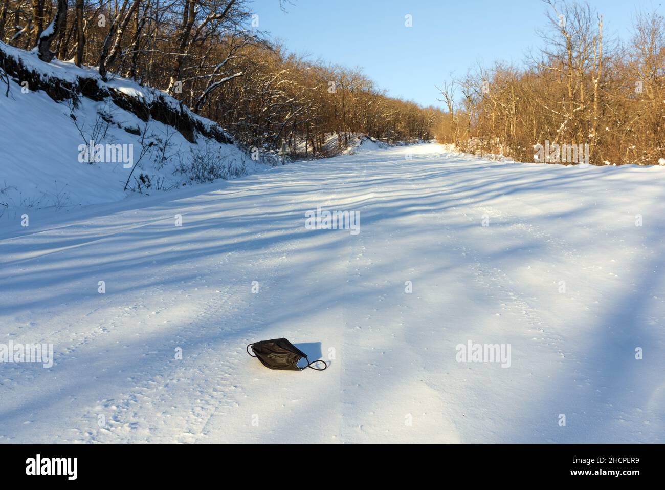 Werfen Einweg-medizinische Maske auf Winterstraße. Verwendung einer hygienischen Maske während einer Pandemie des Corona-Virus. Umweltverschmutzung Stockfoto