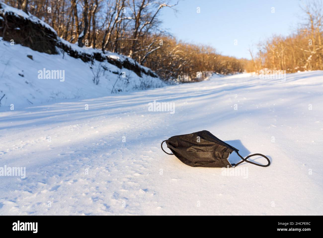 Werfen Einweg-medizinische Maske auf Winterstraße. Verwendung einer hygienischen Maske während einer Pandemie des Corona-Virus. Umweltverschmutzung Stockfoto