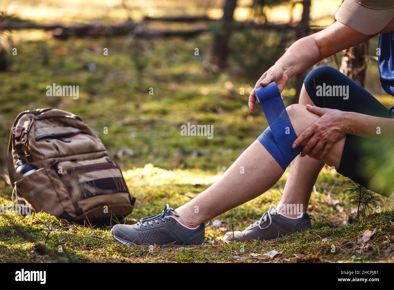 Verletzte Wanderin, die ihr elastische Binde auf das Knie legte. Unfall beim Wandern. Trekking erste Hilfe. Kniegelenkschmerzen und Sehnenprobleme während des Abenteuers Stockfoto