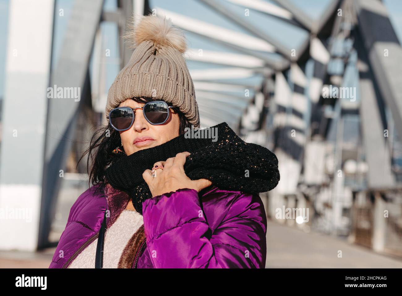 Porträt einer lächelnden Frau mit Sonnenbrille und Wollmütze an einem sonnigen Herbsttag, der durch die Stadt geht Stockfoto