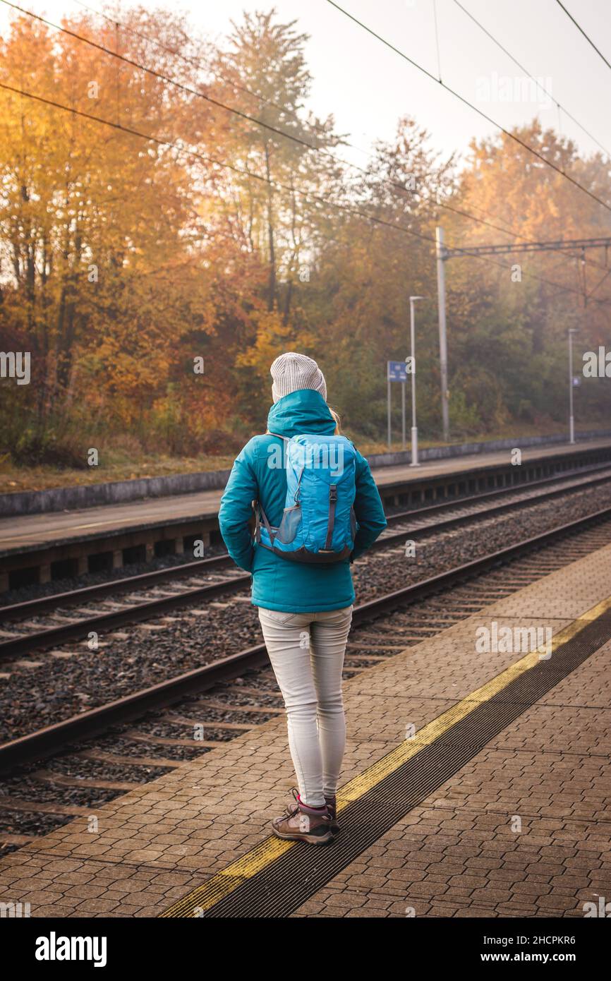 Solo-Tourist mit Rucksack wartet auf Zug am Bahnhofsplatz. Frau, die in der Herbstsaison mit dem Zug unterwegs ist Stockfoto