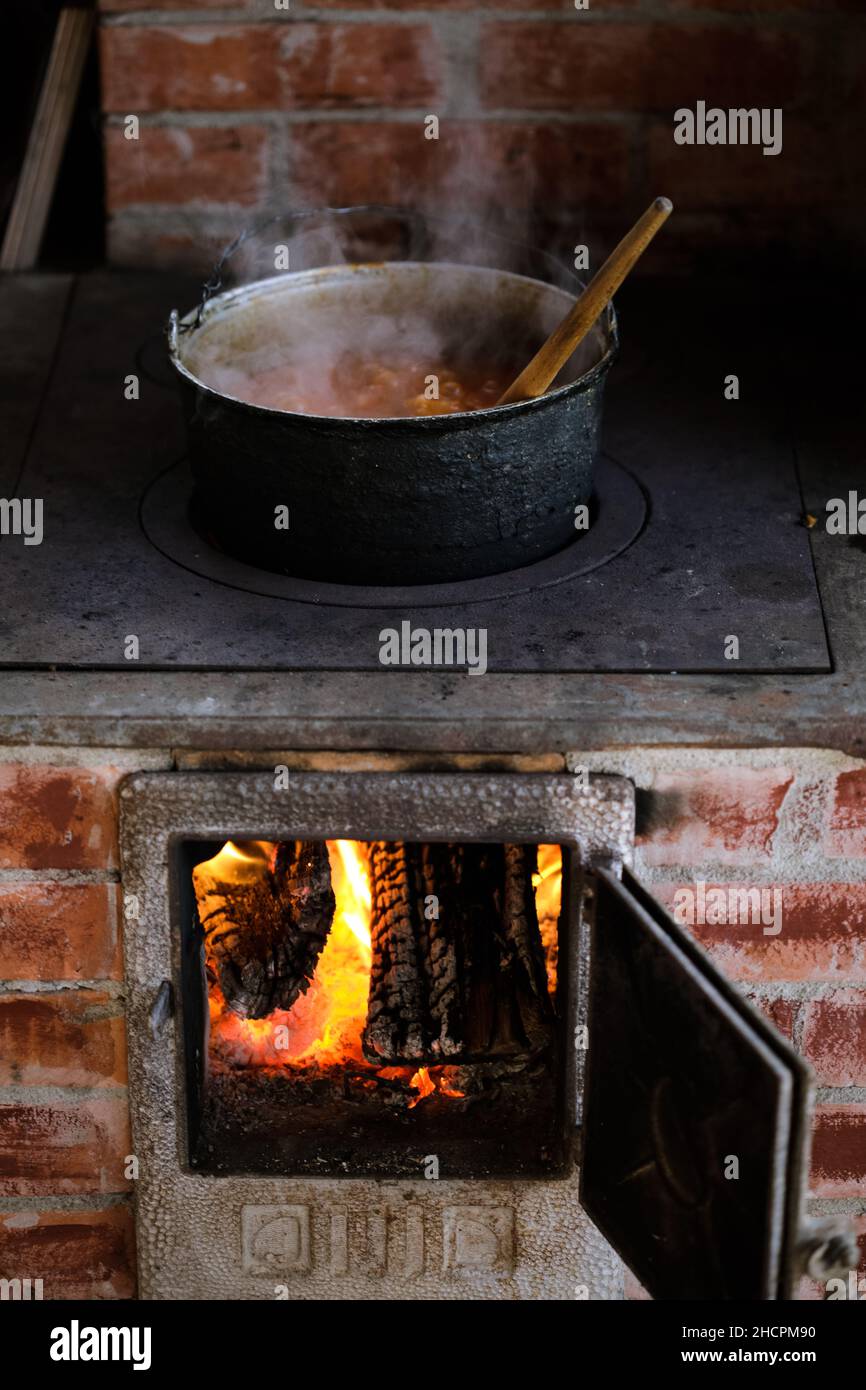 Gusseiserner Kessel kocht einen Gulasch-Eintopf über einem Holzofen aus roten Ziegeln im Hinterhof eines ländlichen Hauses in Rumänien. Stockfoto