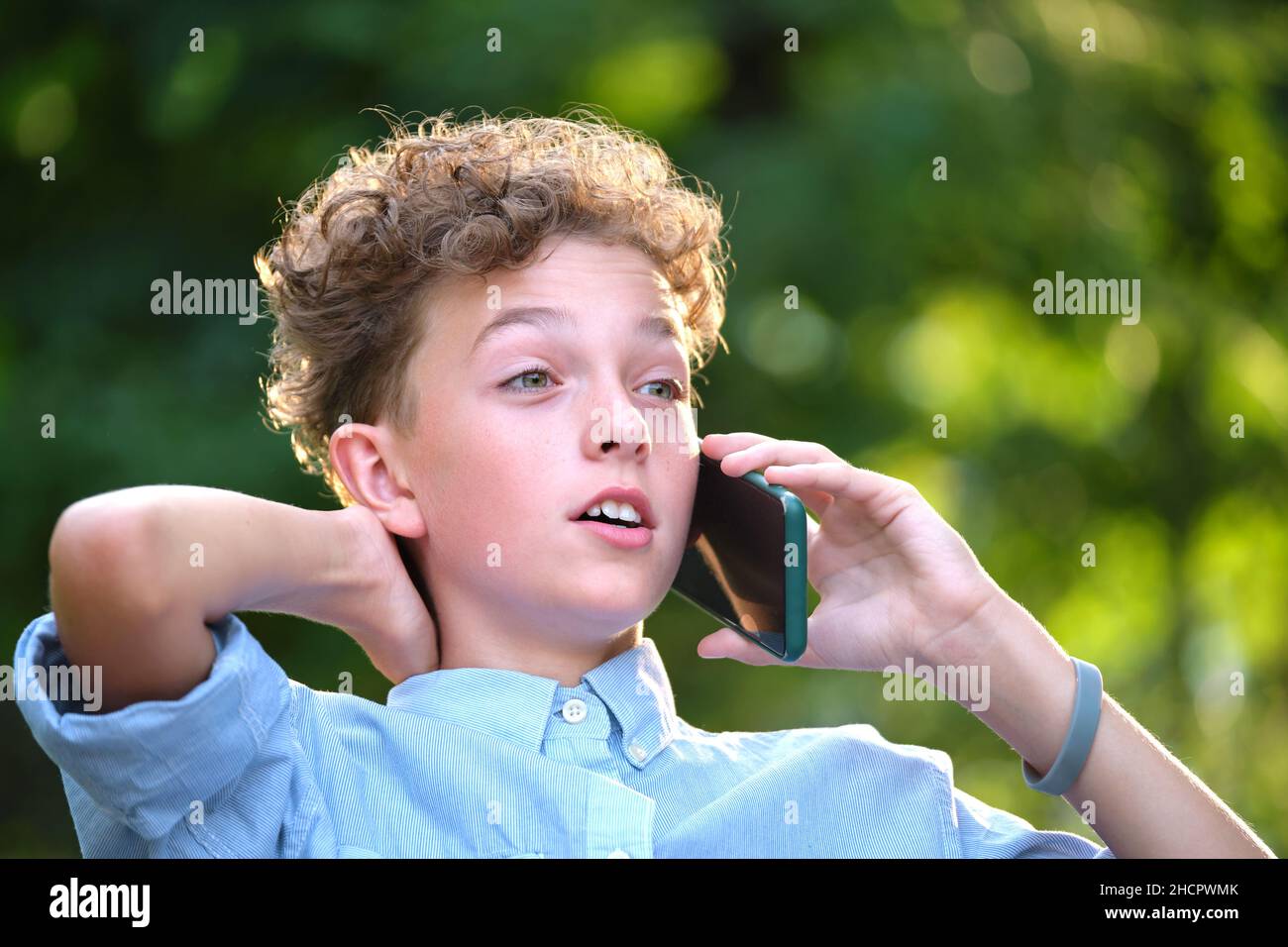 Kleiner Junge, der im Sommerpark mit dem Handy im Gespräch ist. Konfliktsituationen im Teenageralter Konzept. Stockfoto