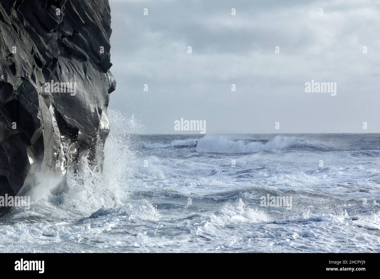 Eine felsige Felswand, die von mächtigen Wellen in der Nähe von Dyrhólaey glatt getragen wird. Island. Stockfoto