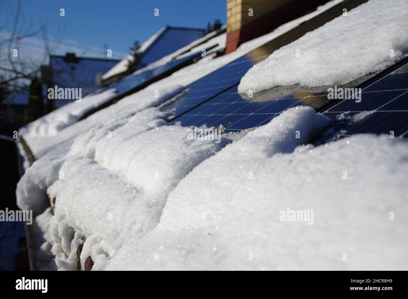 Sonnenkollektoren von Schnee bedeckt. Photovoltaikanlage auf dem Hausdach während der Wintersaison an einem sonnigen Tag. Alternative PV-Energie-Produ Stockfoto