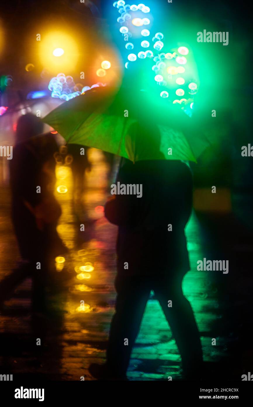 Ein Mann, der von einem grünen Regenschirm geschützt wird, der inmitten eines Sturms eine Straße überquert. Stockfoto