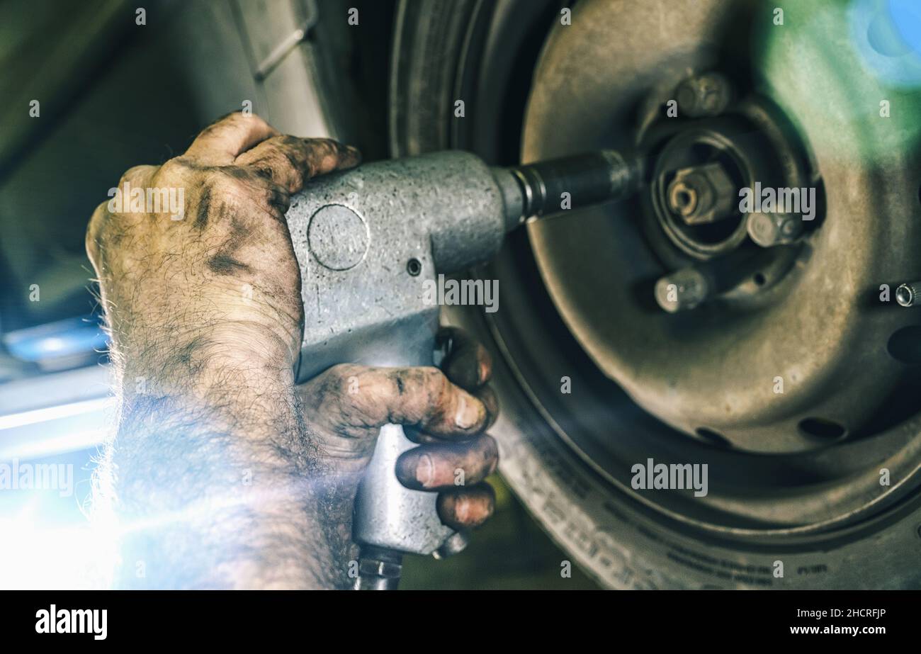 Automechaniker beim Wechseln eines Autoreifens in der Werkstatt für Mechaniker und beim Lösen der Schrauben mit einer elektrischen Bohrmaschine. Reparaturservice. Authentische Nahaufnahme Stockfoto