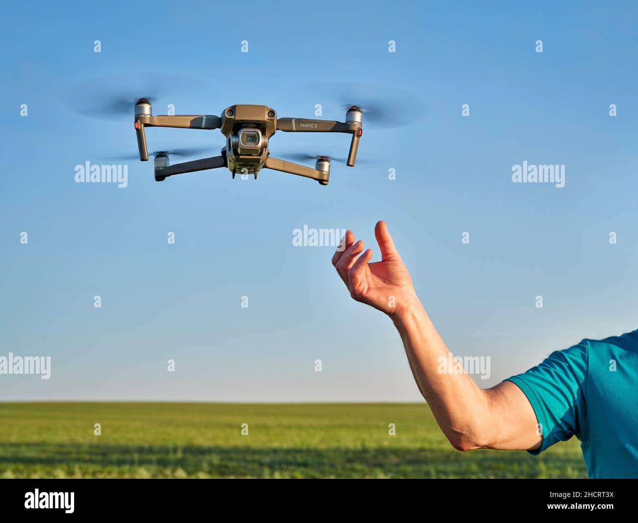 New Raymer, CO, USA - 8. Juni 2021: Eine Pilot Hand und eine DJI Mavic 2 Pro Quadcopter Drohne fliegen über grüne Prärie. Stockfoto