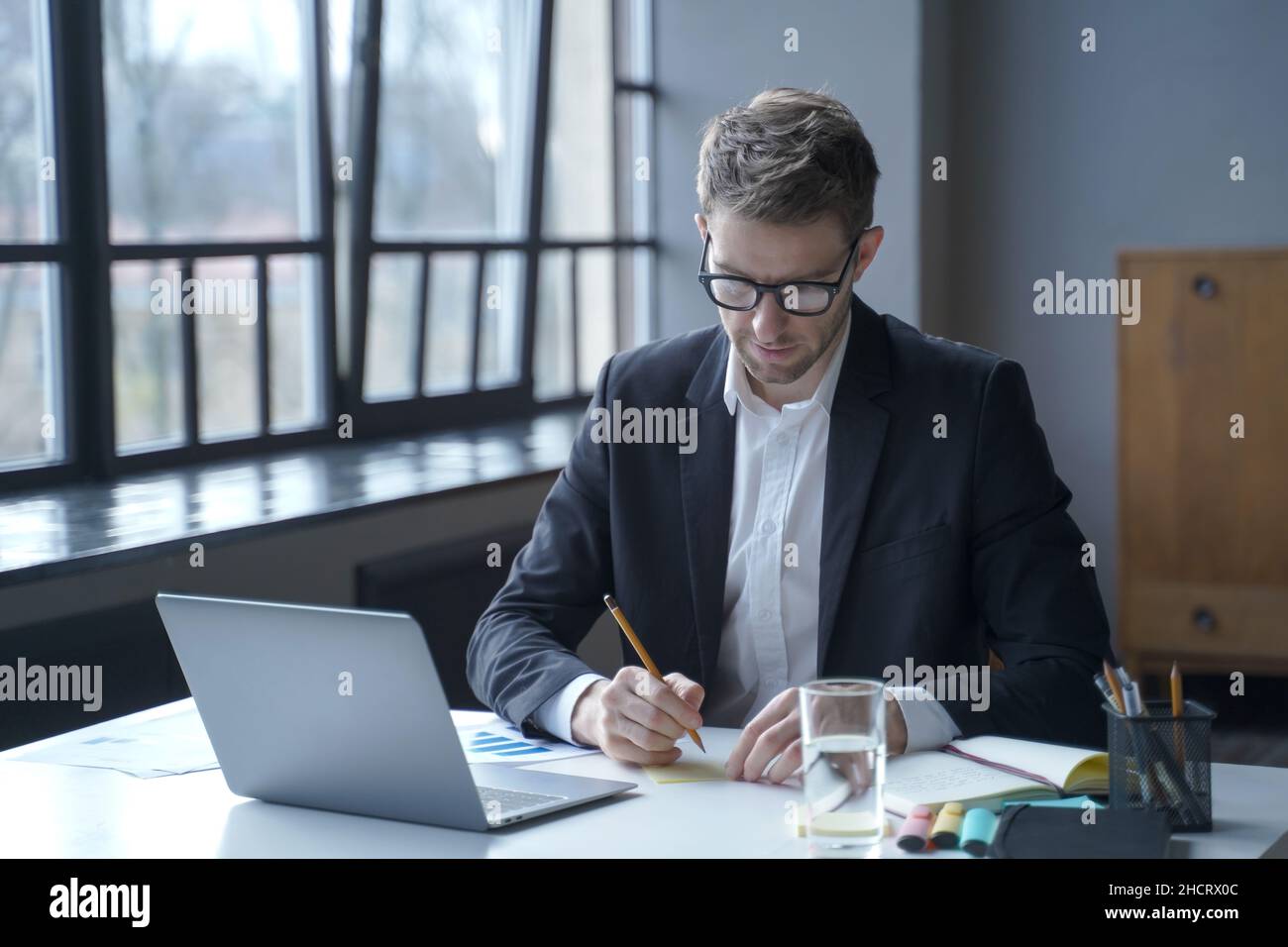 Ein konzentrierter männlicher Bankier schreibt Memos auf Haftnotizen auf, während er von zu Hause aus arbeitet Stockfoto