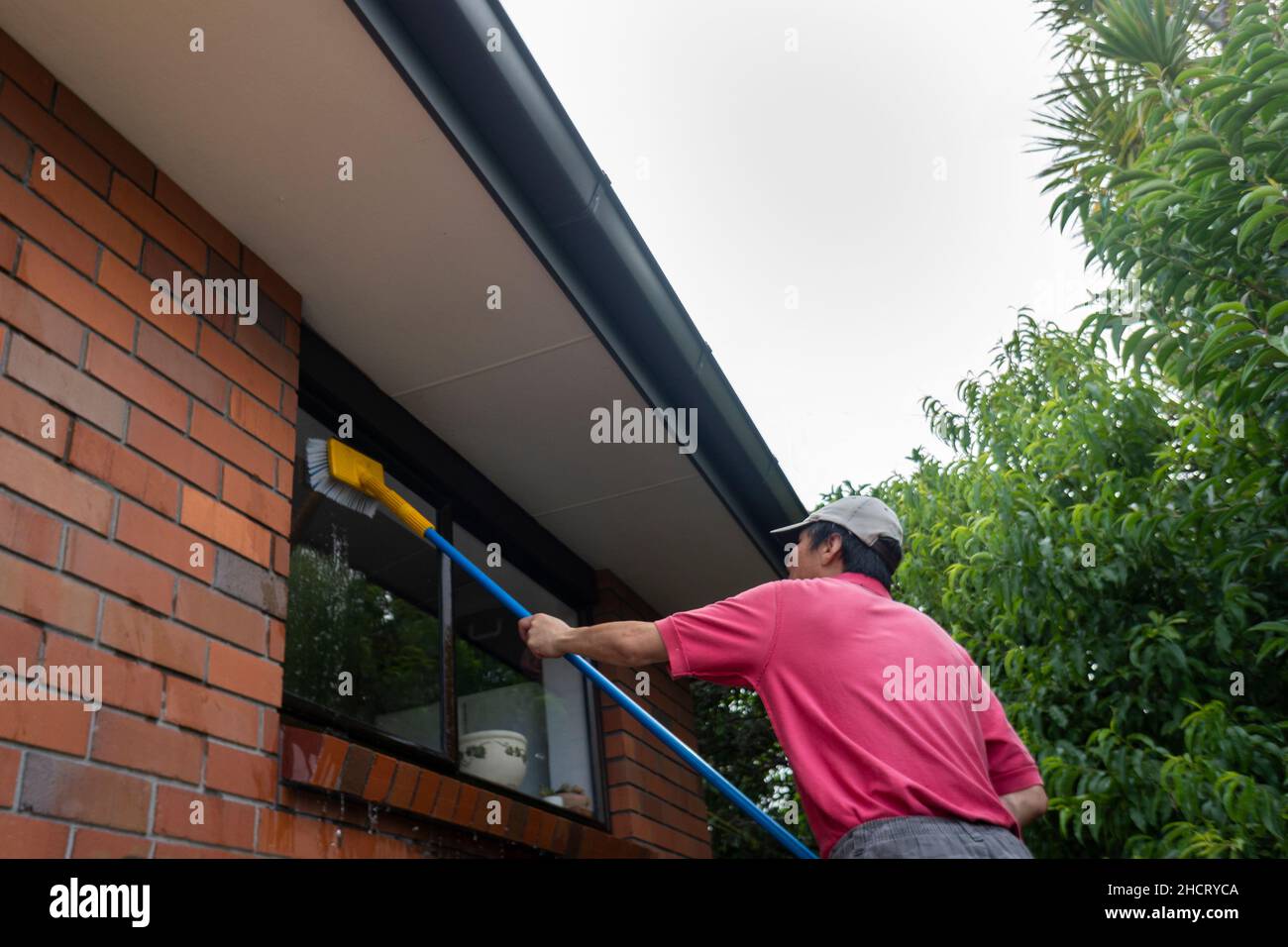 Low-Angle-Ansicht eines Mannes Waschfenster mit langen Stange und Bürste in Auckland Stockfoto