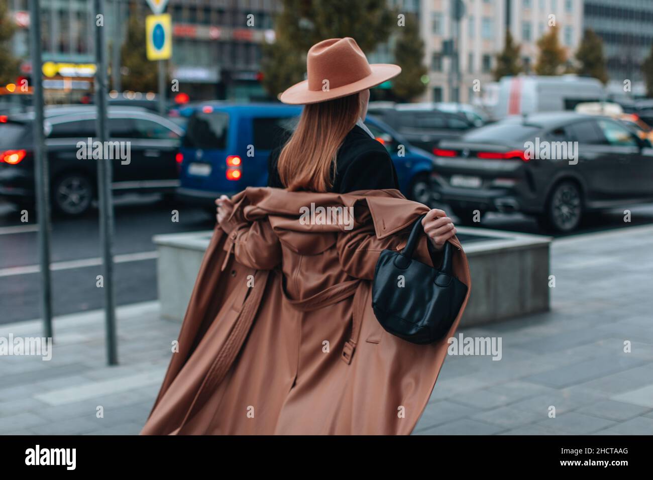 Junge blonde Frau in beigem Hut und langem Herbst braunen Ledermantel zu Fuß in der Stadt. Damenmode im Street-Stil Stockfoto