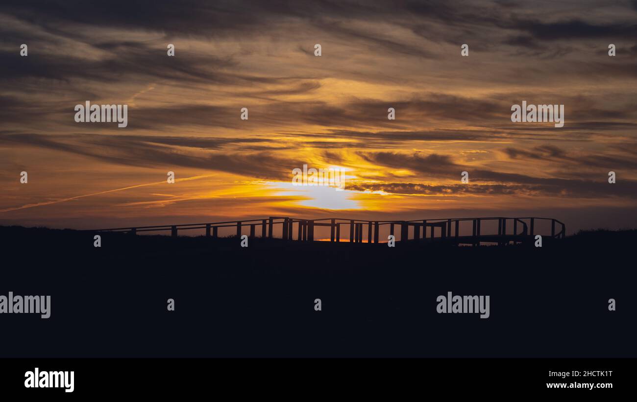 Dunkelgoldener Sonnenuntergang mit dramatisch bewölktem Himmel über der Silhouette der Promenade in Quiaios Beach, Portugal Stockfoto