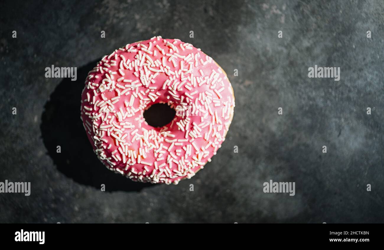 Donut mit rosa glasiert und streut auf einem dunklen Tisch Stockfoto