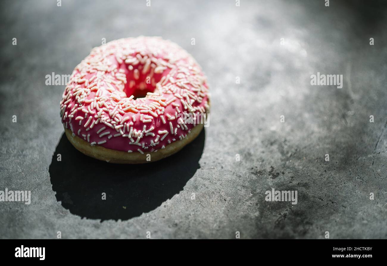 Donut mit rosa glasiert und streut auf einem dunklen Tisch Stockfoto