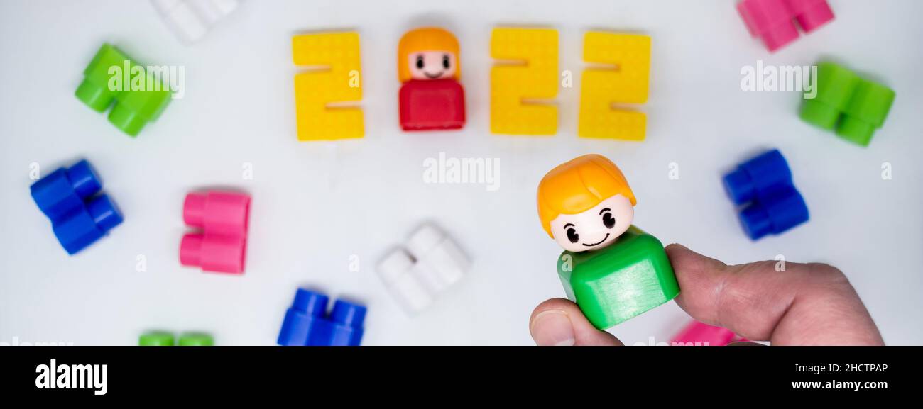 Banner mit Vintage bunten Bausteinen, Spielzeug Kunststoff-Figuren: Mädchen in 2022 Zahlen, Junge in der Hand, weißer Hintergrund. Stockfoto