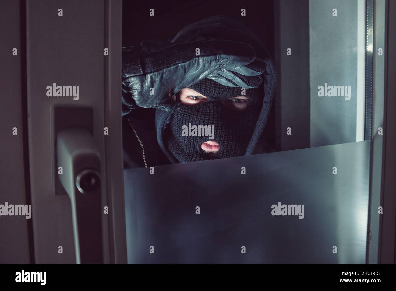 Einbrecher mit Blick durch das Fenster in der Nacht Stockfoto