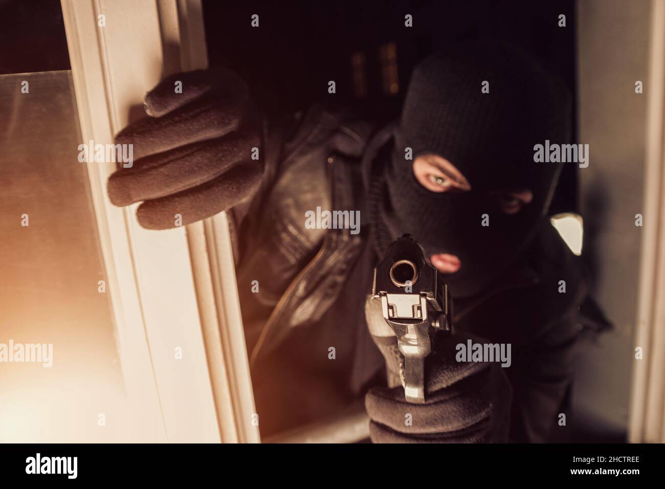 Ein Terrorist oder ein Dieb, der eine Waffe in ein Haus zeigt Stockfoto