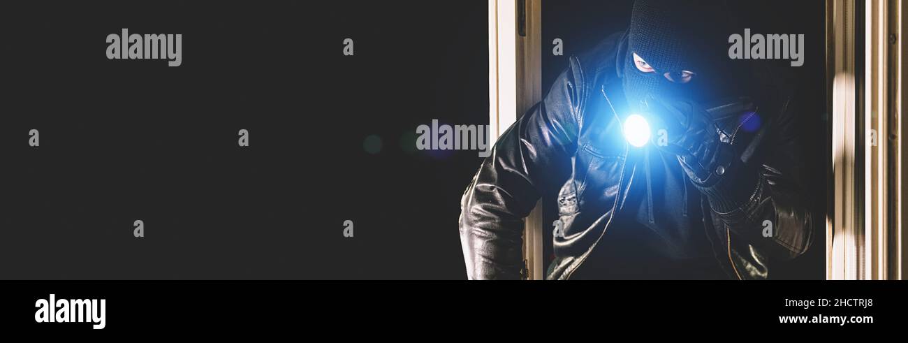 Einbrecher mit Brechstange und Taschenlampe im Fenster eines Hauses, mit Kopierraum, Bannergröße Stockfoto