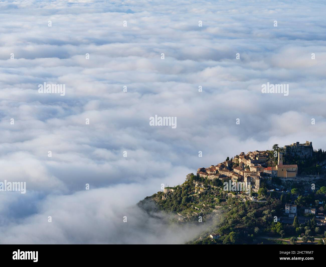 Das mittelalterliche Dorf Èze auf einem Hügel über einem Wolkenmeer. Nebel ist ein sehr seltenes Wetterphänomen an der französischen Riviera. Alpes-Maritimes, Frankreich. Stockfoto