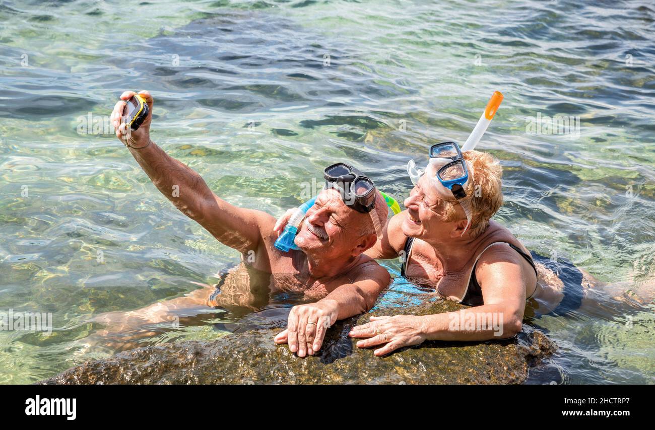 Glückliches Ehepaar im Ruhestand, das Selfie bei einem tropischen Meeresausflug mit Wasserkamera und Schnorchelmaske macht - Bootsfahrt zum Schnorcheln in exotischen Szenarien Stockfoto