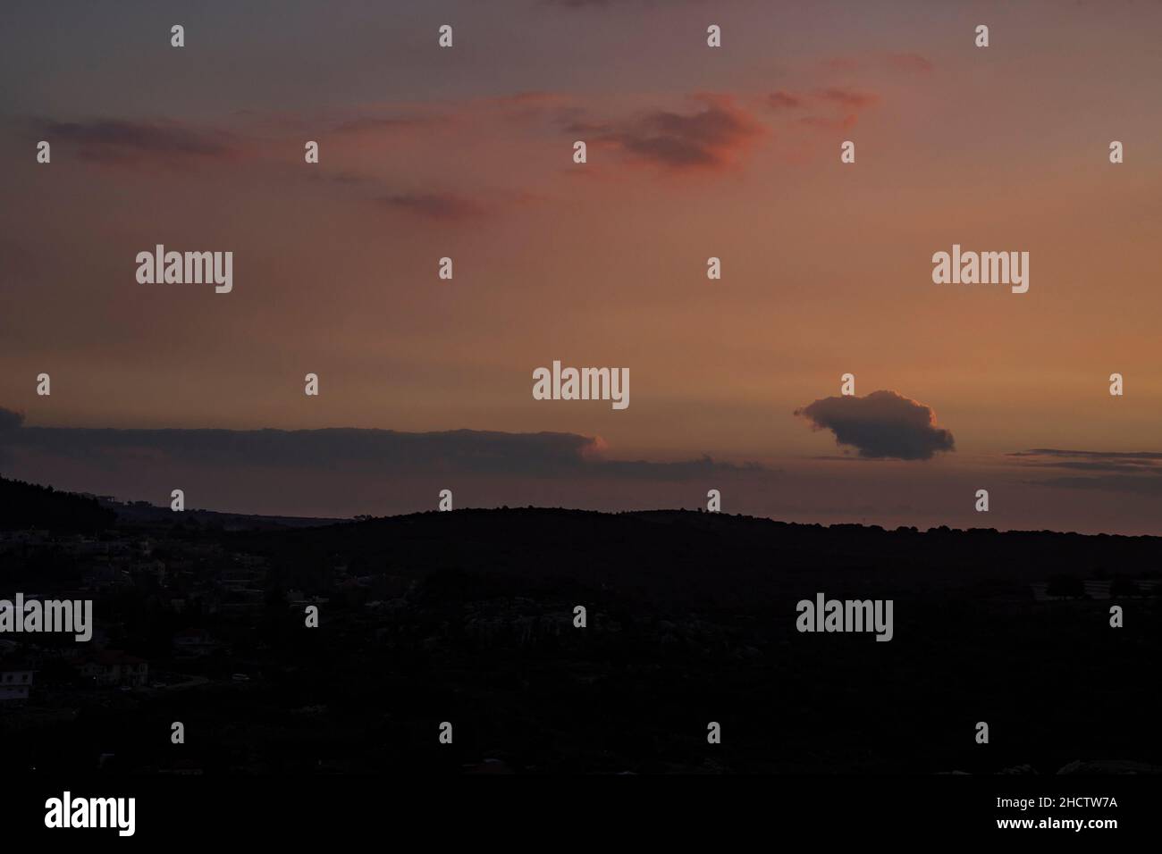 Der teilweise bewölkte Himmel wird bei Sonnenuntergang über einem Dorf in den Galiläischen Bergen, Israel, rot. Stockfoto