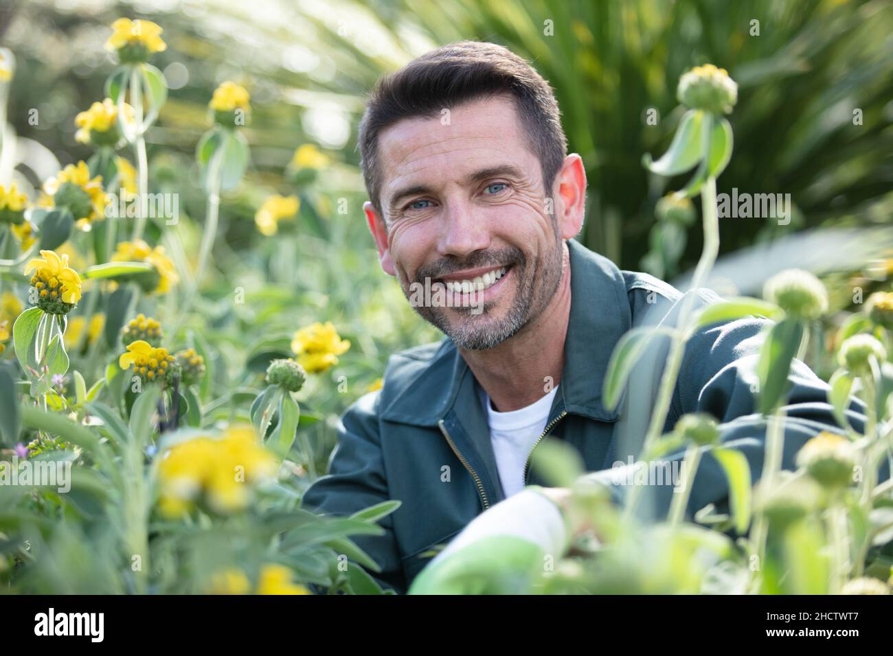 Männlicher Gärtner, umgeben von blühenden Pflanzen Stockfoto