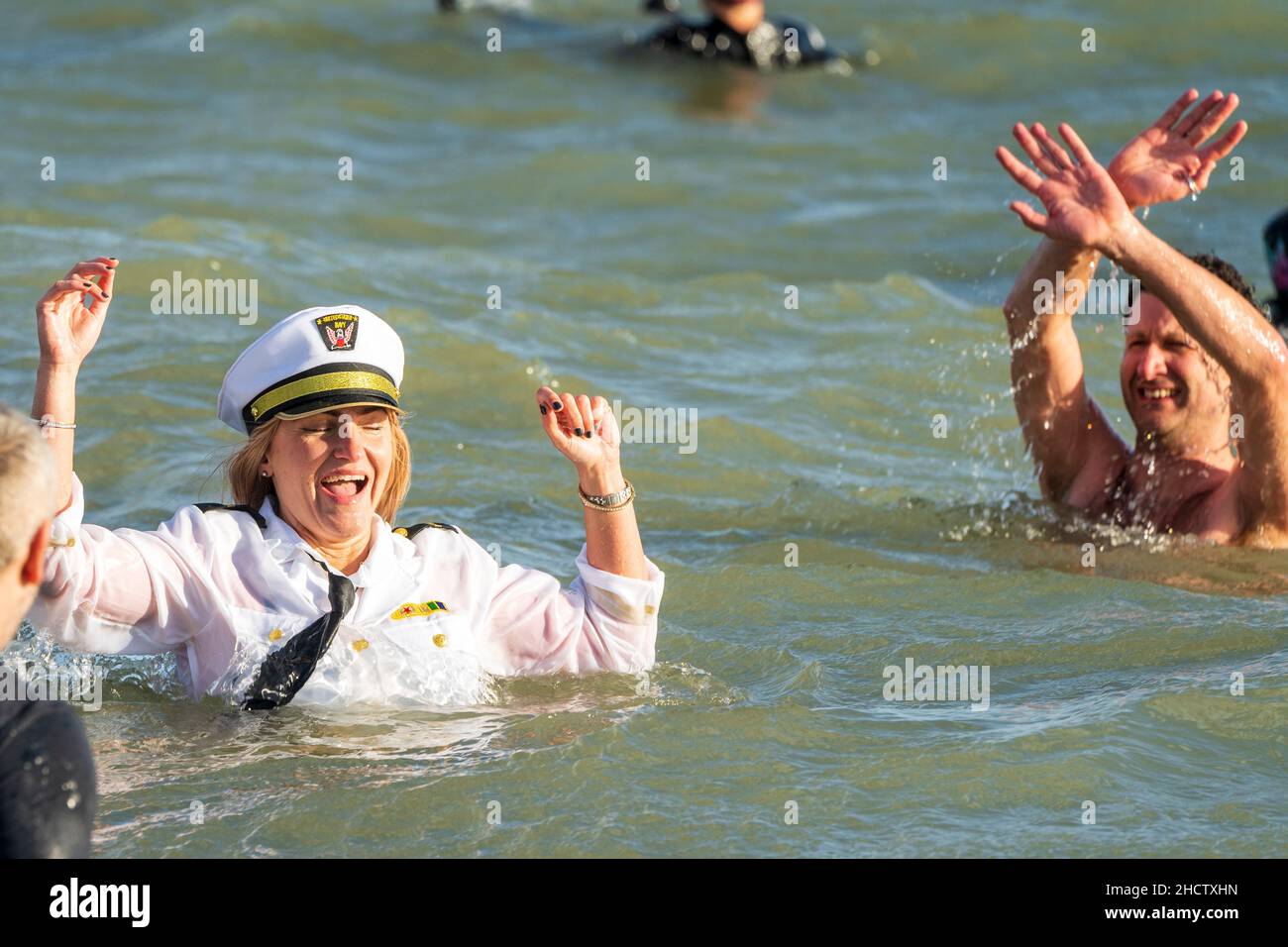 Zwei Frauen, eine in einer Weile Militäruniform, lachen, während sie tief im Meer auf der Brust stehen und die Hände hochwinken. Sie nehmen am Neujahrsschwimmen in Ramsgate an der Küste von Kent Teil. Stockfoto
