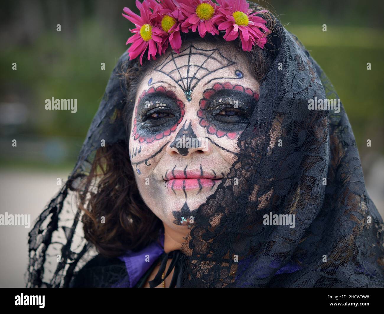 Ernst zu nehmender Mexikanerin mittleren Alters mit Zombie-ähnelichem bemaltem Gesicht-Make-up und schwarzem Schal blickt auf den Zuschauer am Tag der Toten (Dia de los Muertos). Stockfoto