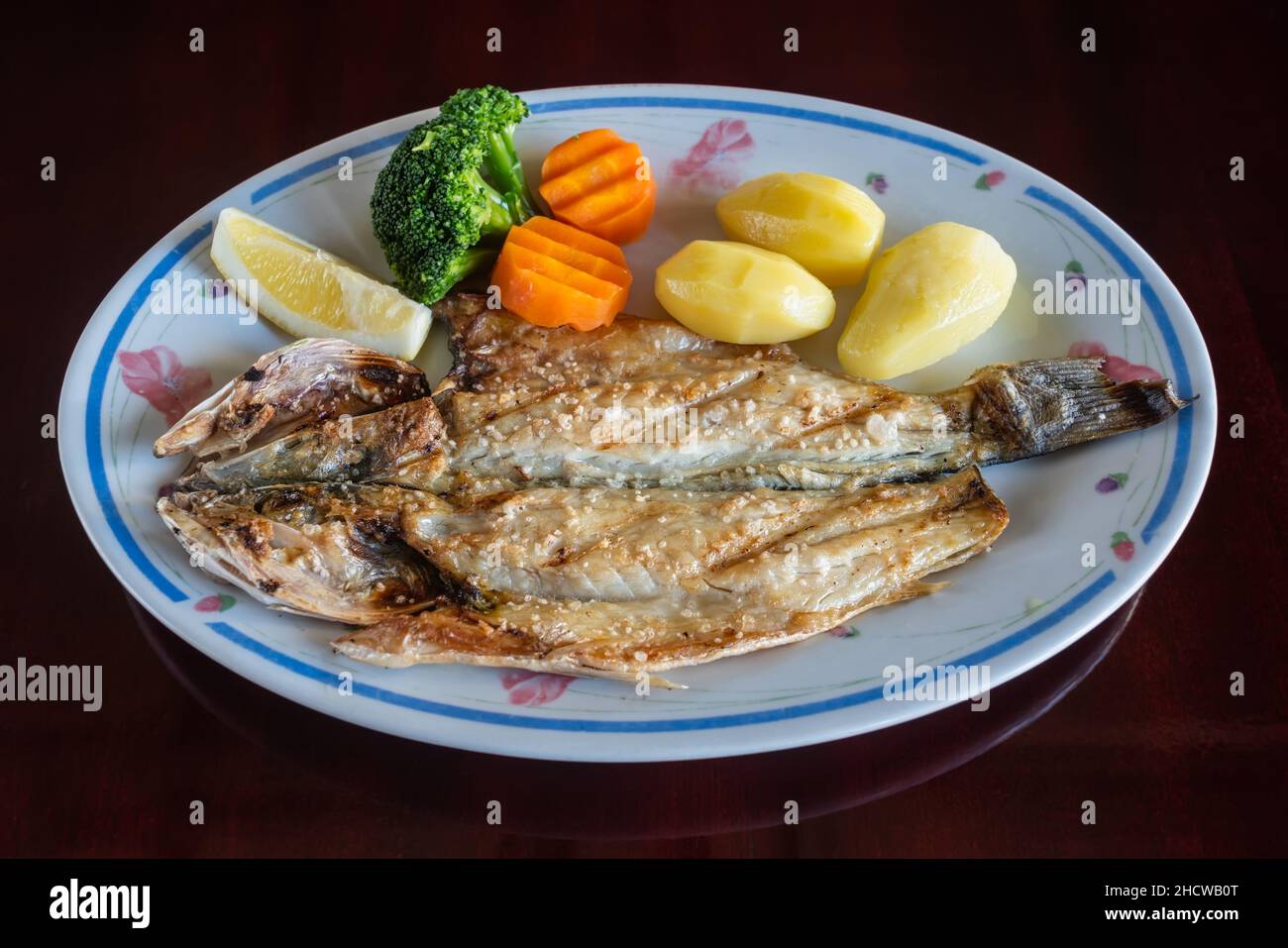 Gegrillter Seebarsch kletterte mit gebackenen Kartoffeln und Gemüse in Teller auf den Tisch. Traditionelles portugiesisches Gericht. Stockfoto