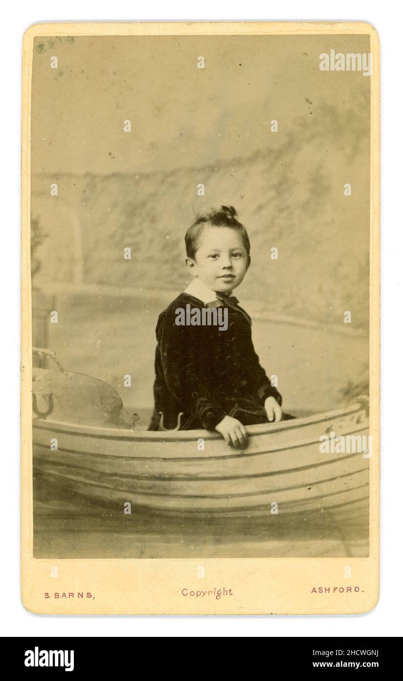 Original viktorianischer CDV mit niedlichem lächelnden Jungen, der in einem Ruderboot sitzt und einen Samtanzug trägt, Fotostudio von S. (Samuel) Barns, Ashford, Kent, England, Großbritannien, datiert 1883 auf der Rückseite. Stockfoto