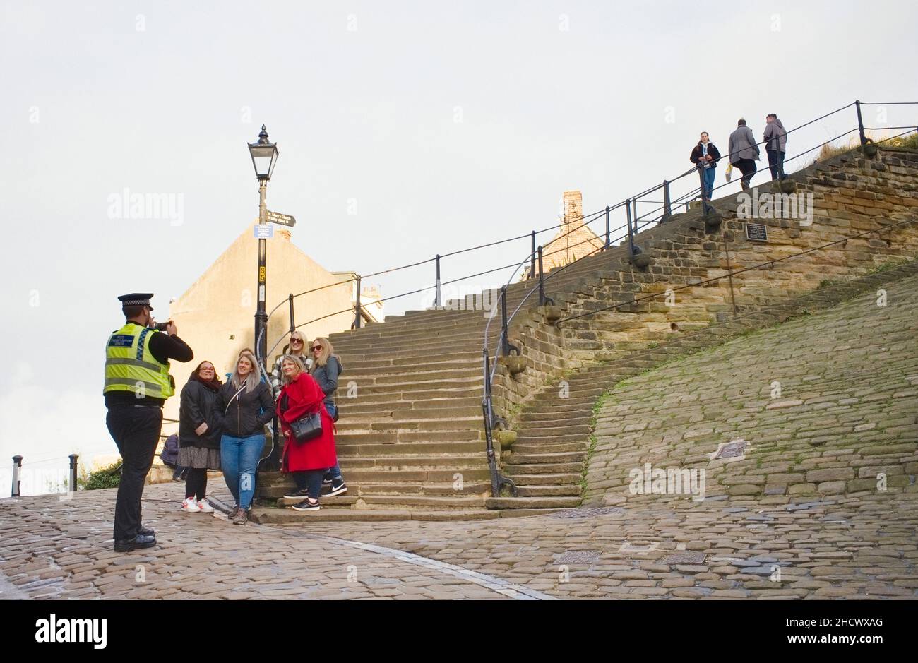 Ein Polizeibeamter macht ein Foto für eine Gruppe von Besuchern von Whitby am Fuße der 199 Stufen, die zur Kirche und Abtei führen. Stockfoto